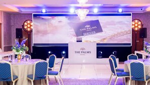 Une salle de conférence à l’hôtel The Palms, avec un grand écran affichant le nom de l’hôtel, des chaises bleues et un pupitre.