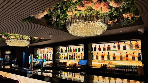 Un espace bar doté d’un comptoir en marbre, d’une variété de bouteilles d’alcool et d’un grand lustre.