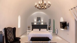 A bedroom with a large bed, a chandelier, a chair, a bench, and a TV mounted on the wall. - Mansion Orny with 2 private pool - My Rental Homes (Fira)