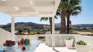 A terrace with a glass table, bottles, and a potted plant, overlooking a mountainous landscape. - Villa Rossini with swimming pool - My Rental Homes (Custonaci)
