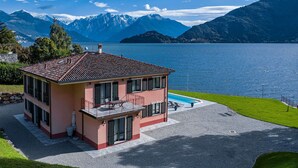 A two-story house with a balcony, a swimming pool, and a view of a lake with mountains in the background.