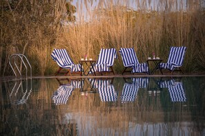 A poolside area with four striped lounge chairs and a small table with a vase.