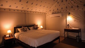 A hotel room with a bed, two bedside tables with lamps, a desk with a chair, an air conditioning unit, and a wall-mounted light fixture. - Impian Resort (Jodhpur)