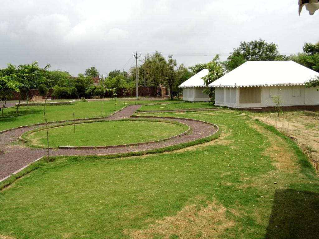 A grassy area with a curved pathway leading to a white tent-like structure.