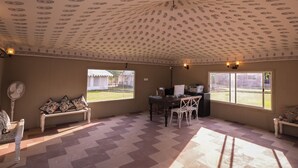 A spacious room with a patterned ceiling, large windows, a dining table with chairs, and a bench. - Impian Resort (Jodhpur)