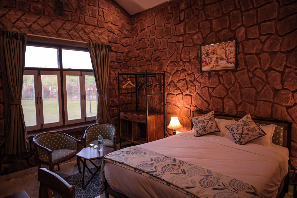 A room with a stone wall, a bed with floral bedding, a table with chairs, and a window with curtains.