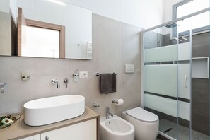 A modern bathroom with a large oval sink, a toilet, and a glass-enclosed shower. - Il Palmeto with private pool - My Rental Homes (Noto)