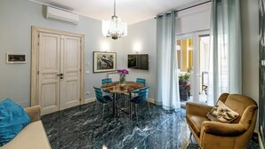 A modern living room with a marble floor, a round table with chairs, a brown leather armchair, and a chandelier. - Tu chiamale emozioni  3 suites (Rome)