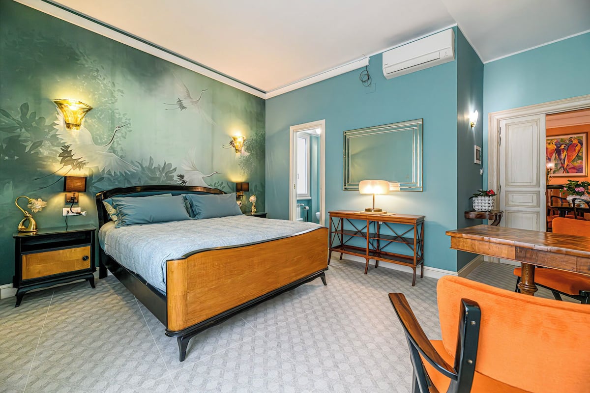 A bedroom with a bed, bedside tables, a dresser, a mirror, and a dining area with chairs and a table.