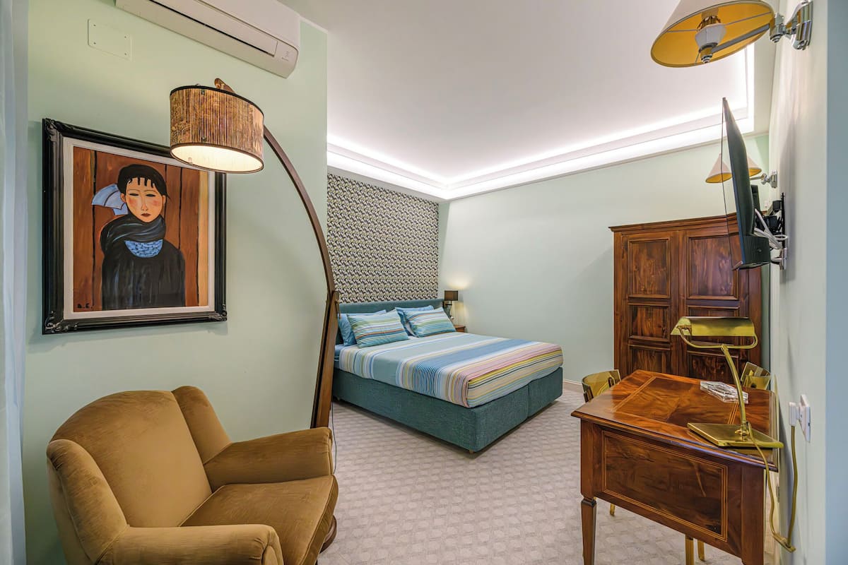 A bedroom with a bed, a desk, a chair, a lamp, and a framed picture on the wall.