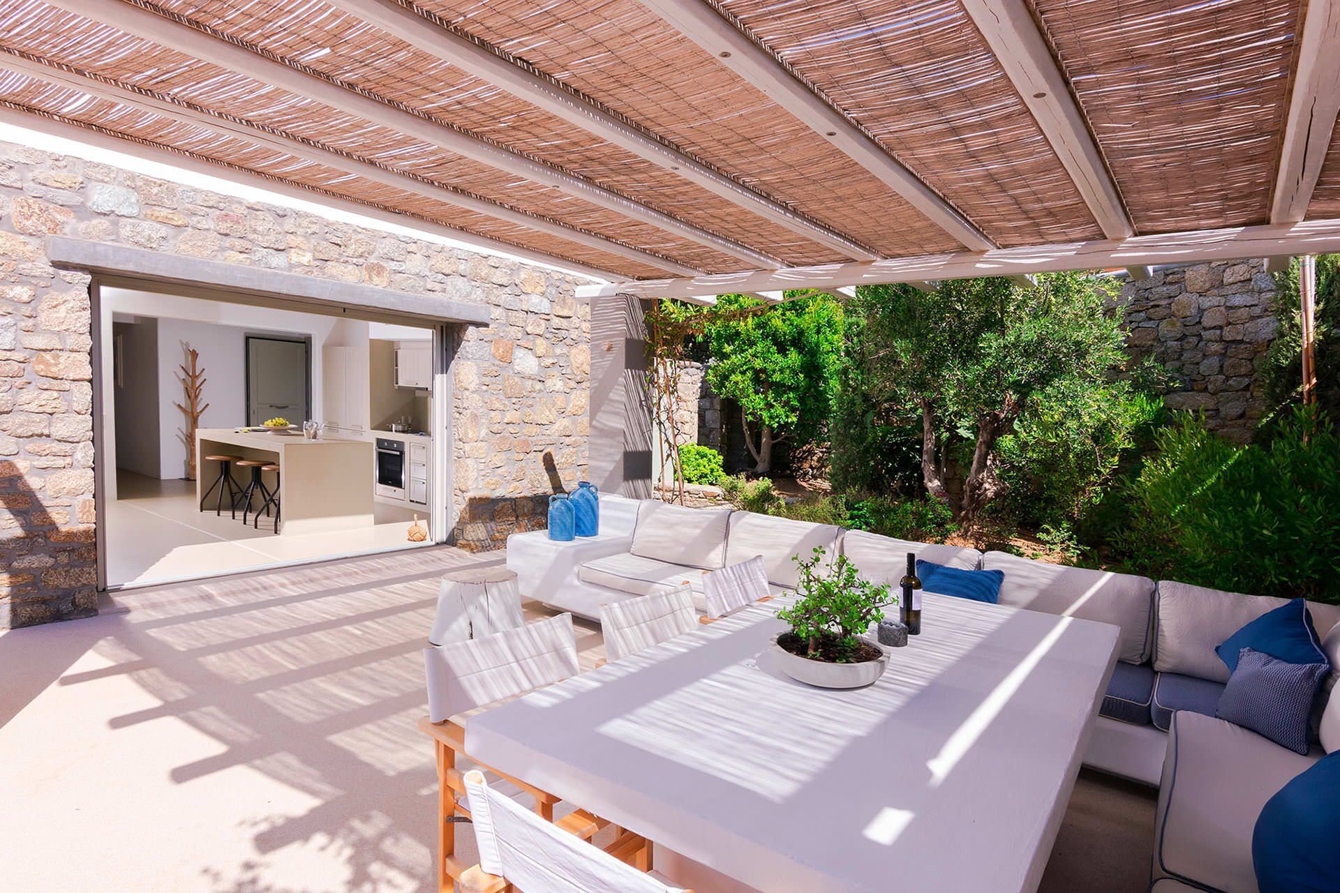 An outdoor patio with a stone wall, a covered seating area, and a view of the kitchen.