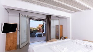 Een moderne slaapkamer met een bed, een televisie en een schuifdeur naar een buitenruimte met uitzicht op zee.