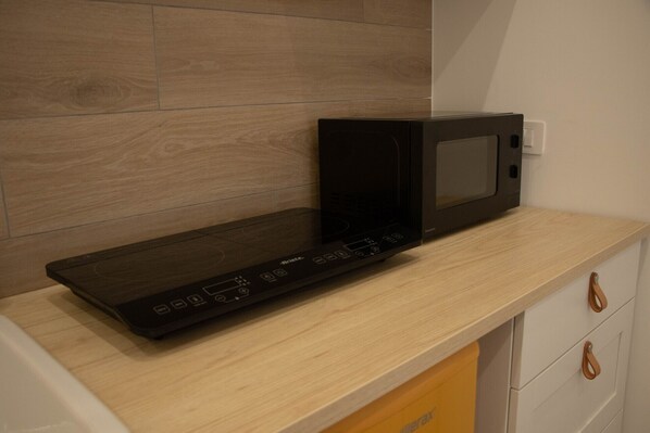 A kitchen with a microwave on a wooden countertop, a white cabinet with a handle, and a light switch on the wall.