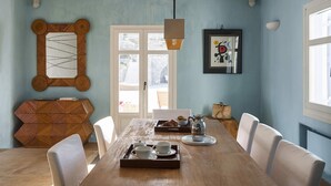 Une salle à manger avec une table en bois mise pour le thé, un buffet en osier et un tableau abstrait encadré.
