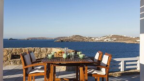 A wooden table with chairs and a view of the sea and hills. - My Rental Homes - Efkalia with infinity pool, panoramic views and private dock (Mykonos)