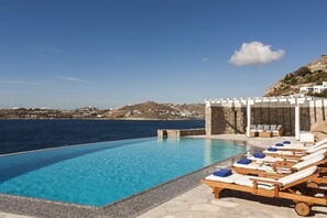 Zona de piscina con sillones de descanso y una pérgola con vistas al paisaje costero.