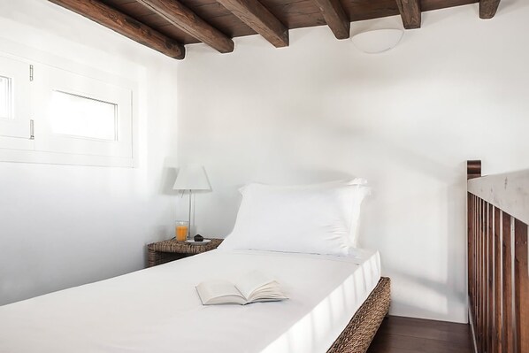 Un dormitorio minimalista con una cama individual, una mesita de noche con lámpara y un libro sobre la cama.
