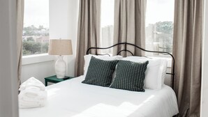 A neatly made bed with white linens and two patterned pillows, a bedside lamp, and a folded towel on a nightstand.