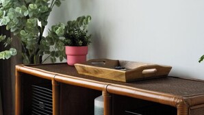 A room with a large window, a flat-screen TV mounted on the wall, a wooden console table with a pink pot and a tray, and a potted plant.
