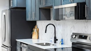 A modern kitchen with dark cabinetry, stainless steel appliances, and a marble backsplash.