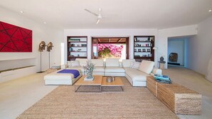 Una sala de estar moderna con un sofá modular, una mesa de centro y un tapete grande. Se observan estanterías y un elemento decorativo en la pared.