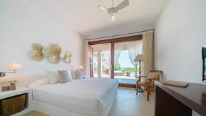 Un dormitorio con cama, mesitas de noche, una silla, un escritorio y vistas al exterior.