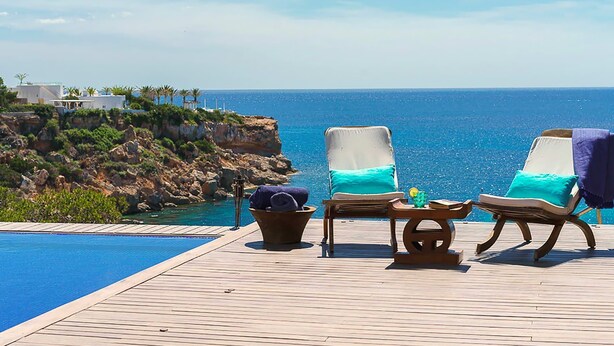 Terraza de madera con dos sillones de descanso frente a una piscina y vista al océano.