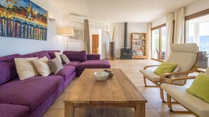 Una sala de estar con un sofá morado, una mesa de centro de madera y un sillón color beige.