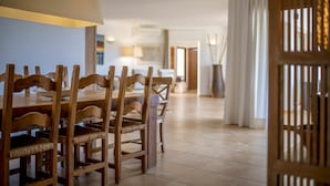 Un comedor con sillas de madera y una mesa, una lámpara, y vistas a una sala con una puerta y cortinas.