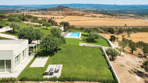 A modern house with a swimming pool, a well-maintained lawn, and a view of distant hills. - Green Hill with pool and terrace - My Rental Homes (Noto)