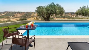 A poolside area with a table and chairs, overlooking a pool and a scenic landscape. - Green Hill with pool and terrace - My Rental Homes (Noto)