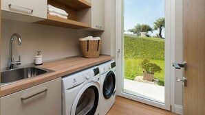 A laundry room with a washing machine, a sink, and shelves with folded towels. - Green Hill with pool and terrace - My Rental Homes (Noto)