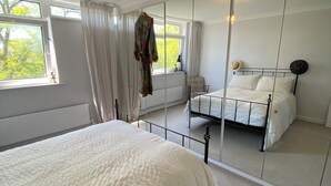 Ein Schlafzimmer mit einem großen Bett, einem Spiegel, einem Kleiderhaken und Blick ins Freie.