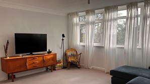 Ein Wohnzimmer mit Flachbildfernseher auf einem Holzkabinett, einer Stehlampe, einem Sessel und einem Sofa.