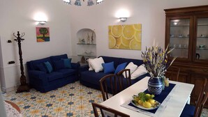 Un salon avec un canapé bleu, une table à manger ornée d’un vase et de citrons, et un mur décoratif sur lequel est accrochée une peinture représentant une tranche de citron.