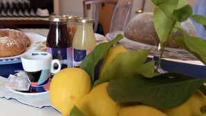 Une table avec une assiette de croissants, un verre de café, un verre de jus de fruits et un verre de lait. On y trouve également deux bouteilles de sirop et un bouquet de citrons.