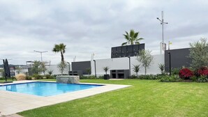 Una piscina con solárium empedrado, rodeada de césped cuidado y diversas plantas.