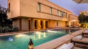 A modern building with a swimming pool, lounge area, and outdoor seating. - My Rental Homes - Villa Noria with garden and private pool (Marrakesh)