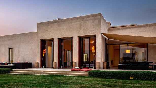 A modern building with large glass doors, a covered outdoor seating area, and a well-maintained lawn. - My Rental Homes - Villa Noria with garden and private pool (Marrakesh)