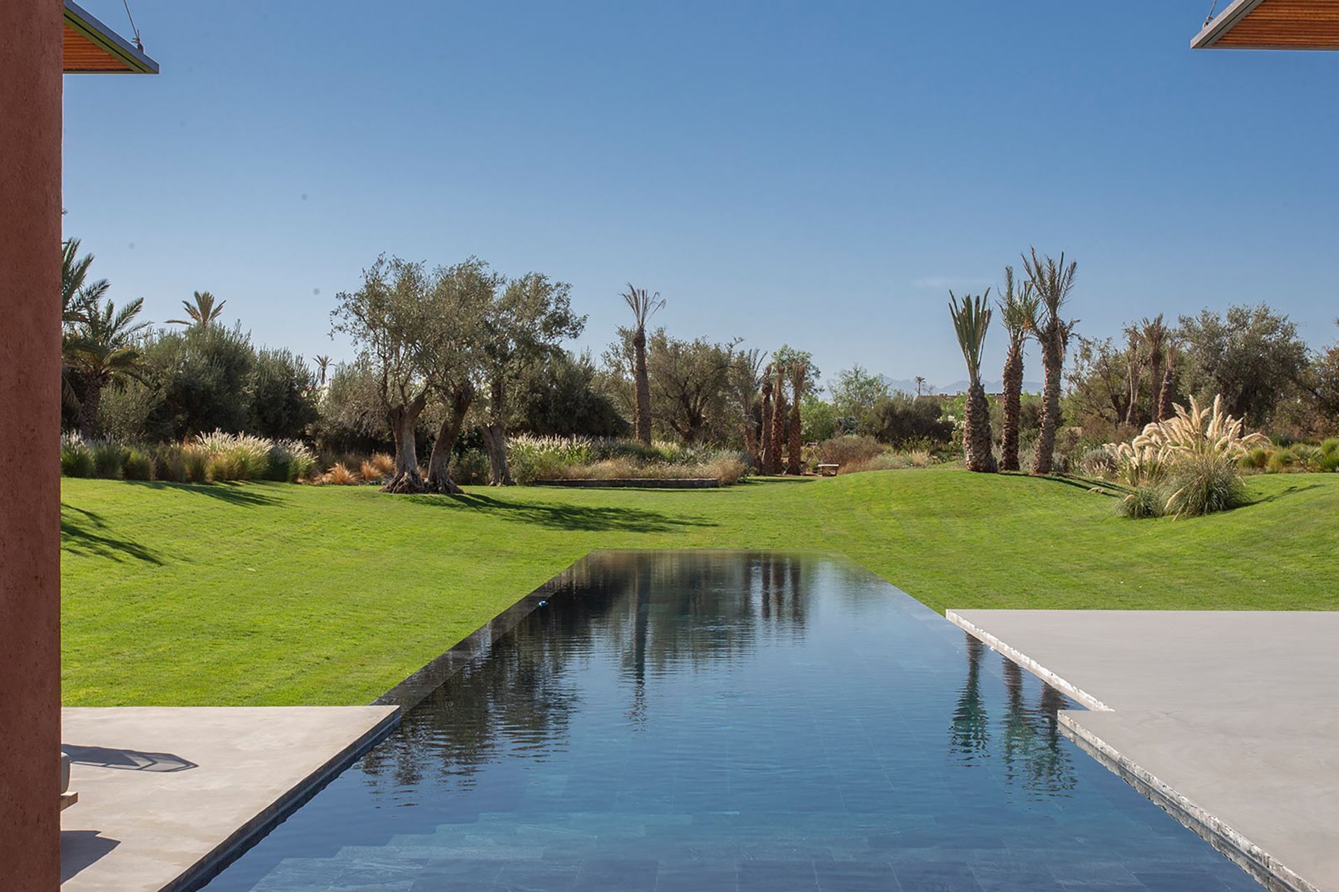 Une piscine offrant une vue dégagée sur le paysage environnant, avec notamment de l’herbe, des arbres et une chaîne de montagnes au loin.