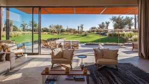 A modern living room with a large glass wall, wicker furniture, and a view of a landscaped garden.