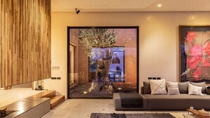 A modern living room with a large glass door leading to a dining area, a grey sofa with cushions, and a black rug.