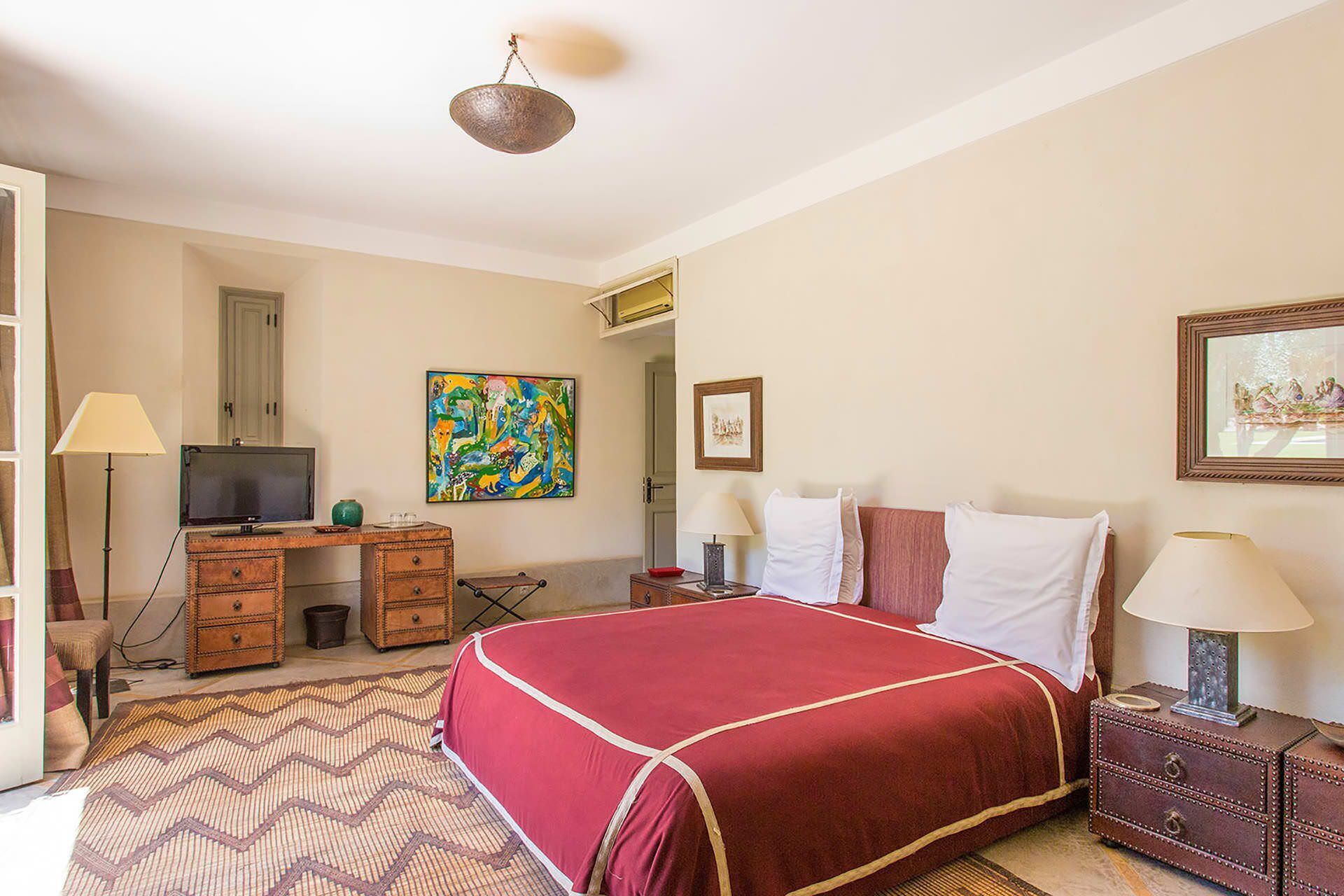 A hotel room with a bed, a desk, a chair, a television, and artwork on the walls.