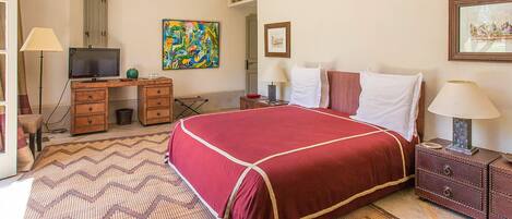 A hotel room with a bed, a desk, a chair, a television, and artwork on the walls.