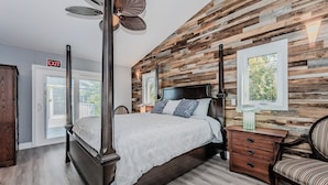 Quarto com cama de dossel, painel de parede em madeira, mesa de cabeceira, cadeira e placa de saída.