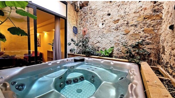 A hot tub in a rustic outdoor setting with a stone wall backdrop.