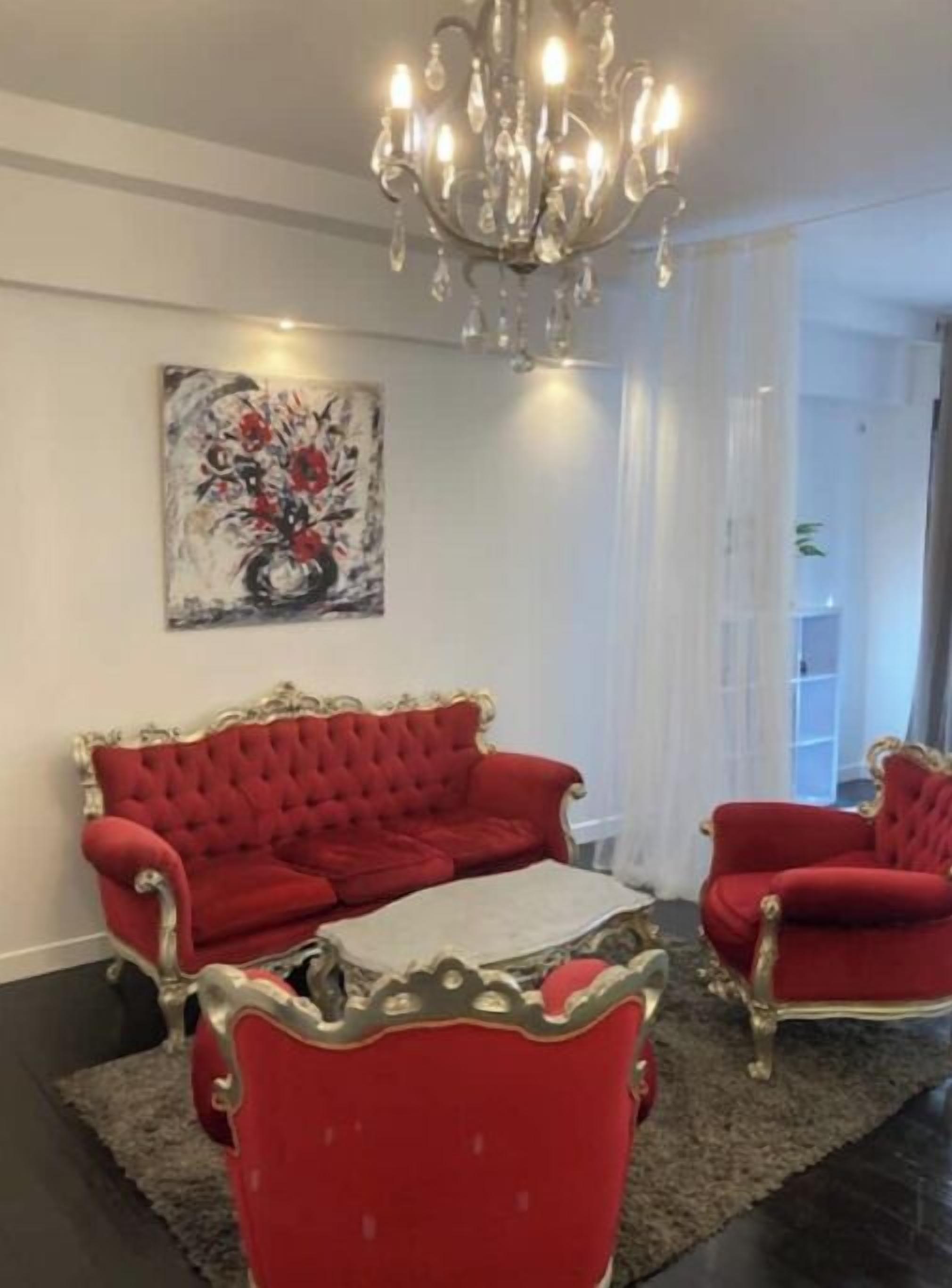 Un salon avec un ensemble de meubles rouges, dont un canapé, un lustre et un tableau accroché au mur.