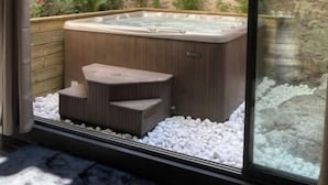 A modern spa area with a hot tub, seating, and a stone wall backdrop.