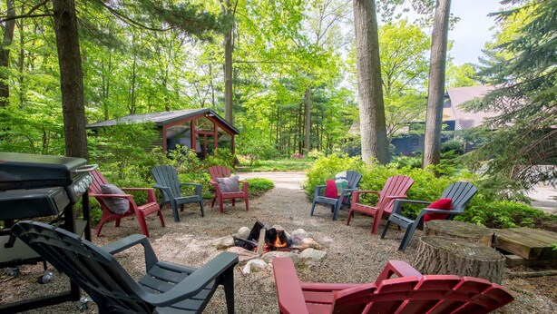 Ein bewaldetes Freigelände mit Adirondack-Stühlen, einer Feuerstelle und einer kleinen Holzhütte.