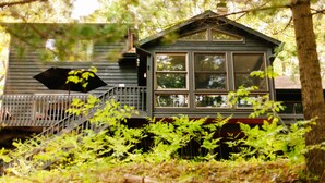 Eine Hütte mit Veranda, Treppe und einem Fenster mit Blick auf einen Wald.